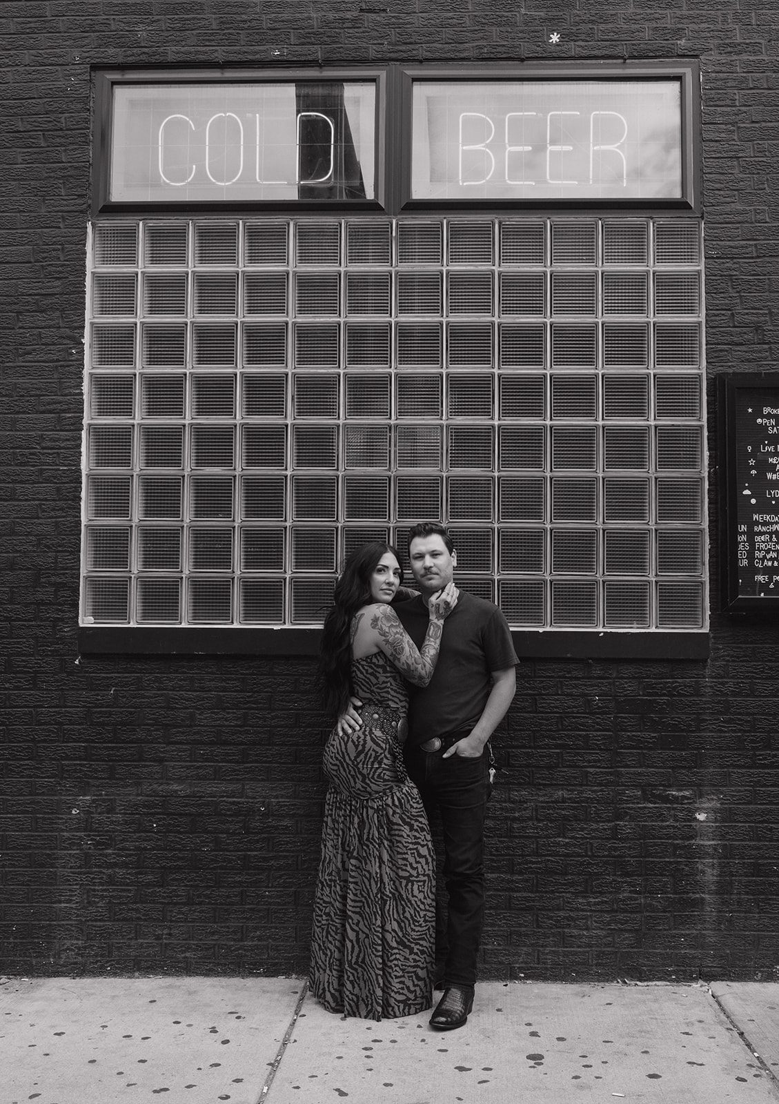 A couple posing for their couples photoshoot in front of a black wall on the outside of a bar
