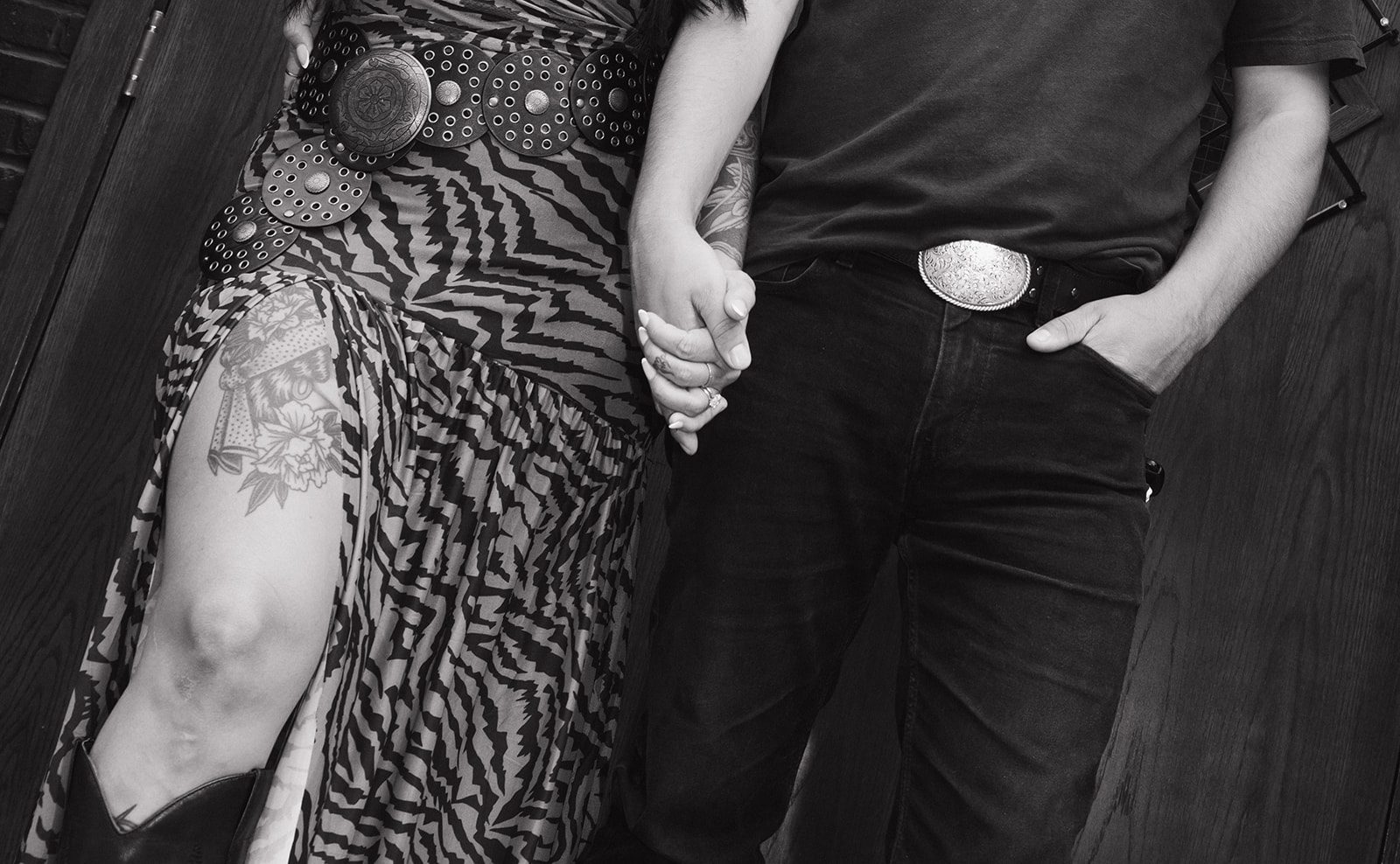 An up-close photo of a couple's unique couples photoshoot outfits, with the man in all black and the woman in a tiger print dress