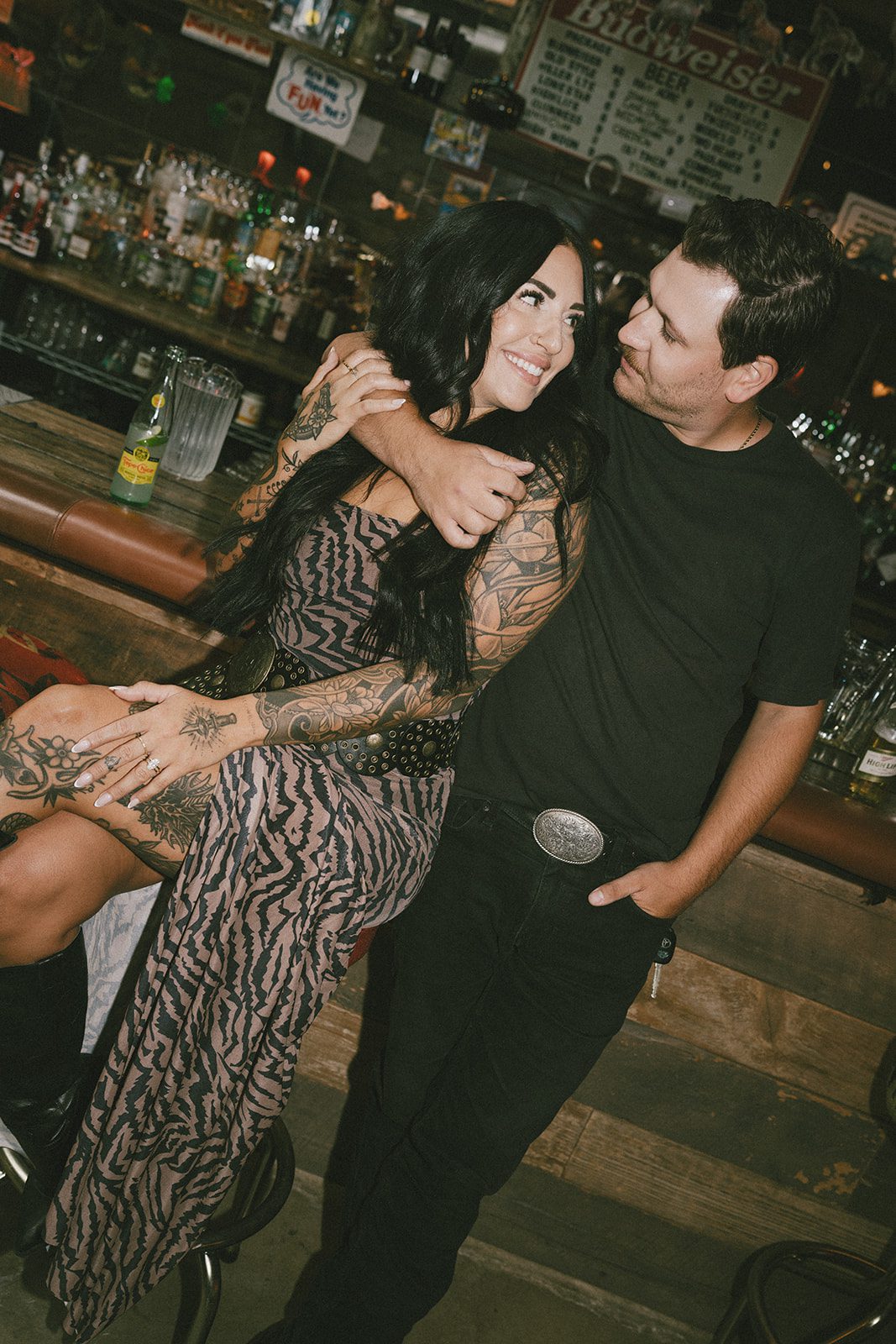 A couple smiling at each other at a bar during their couples photoshoot