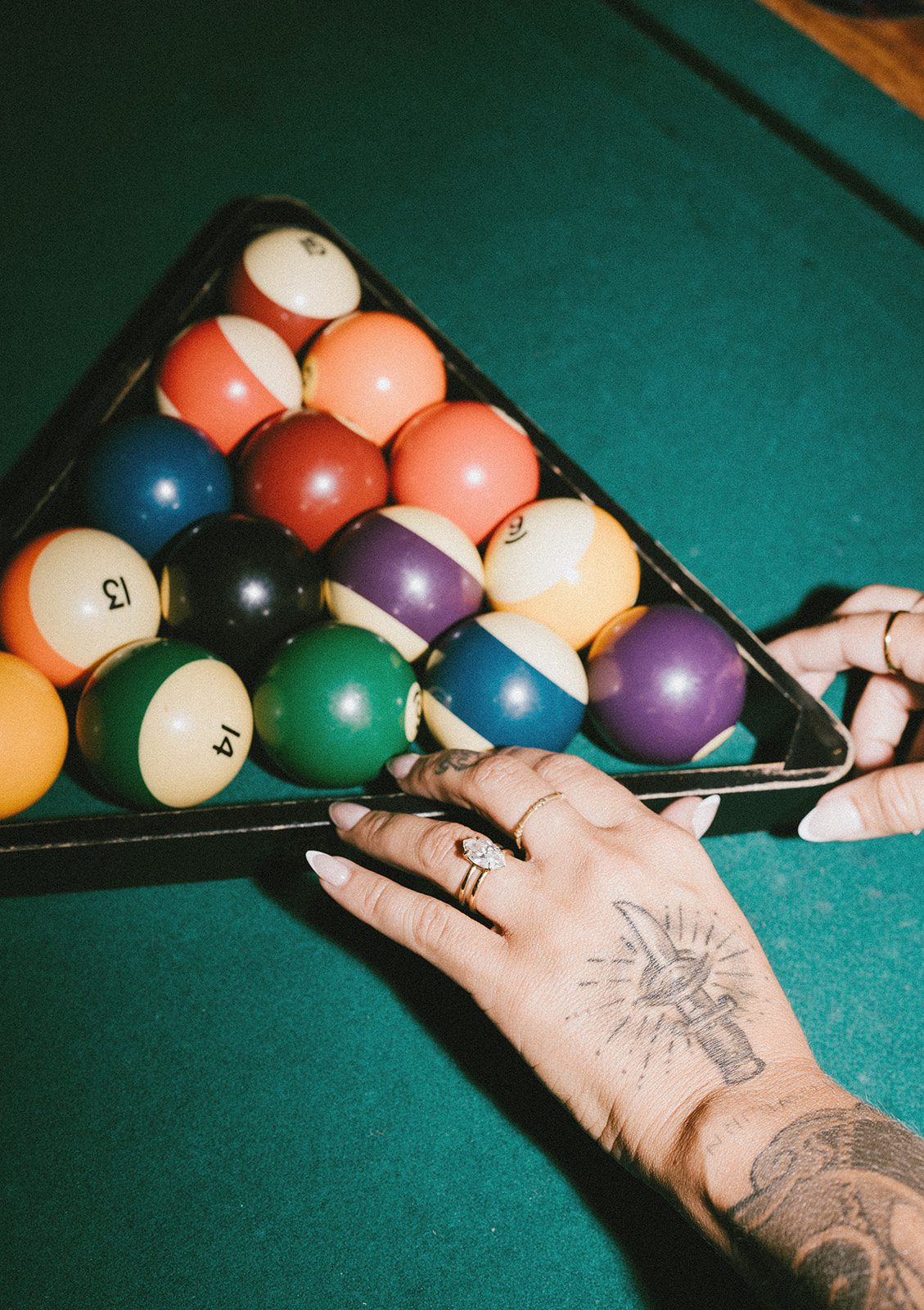 A girl fixing the pool balls at a bar, showing off her engagement ring
