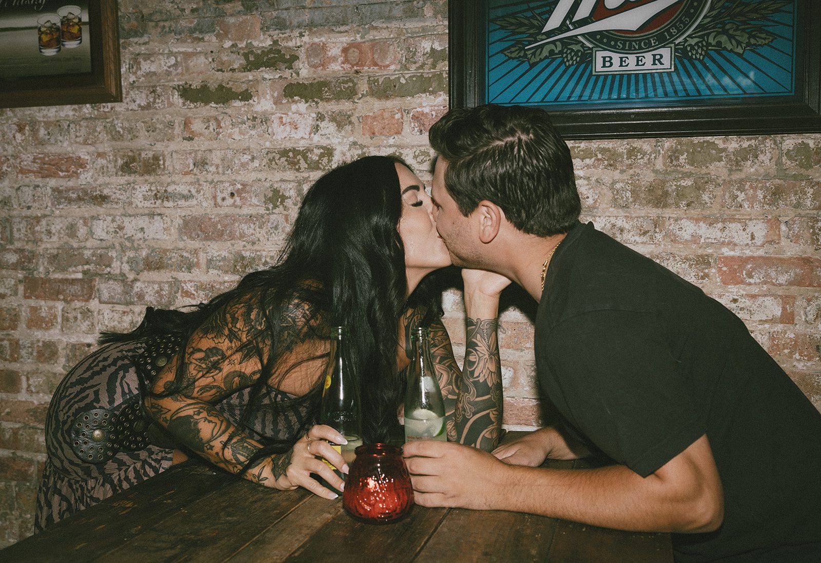 A couple kissing across their table during their couples photoshoot at a bar