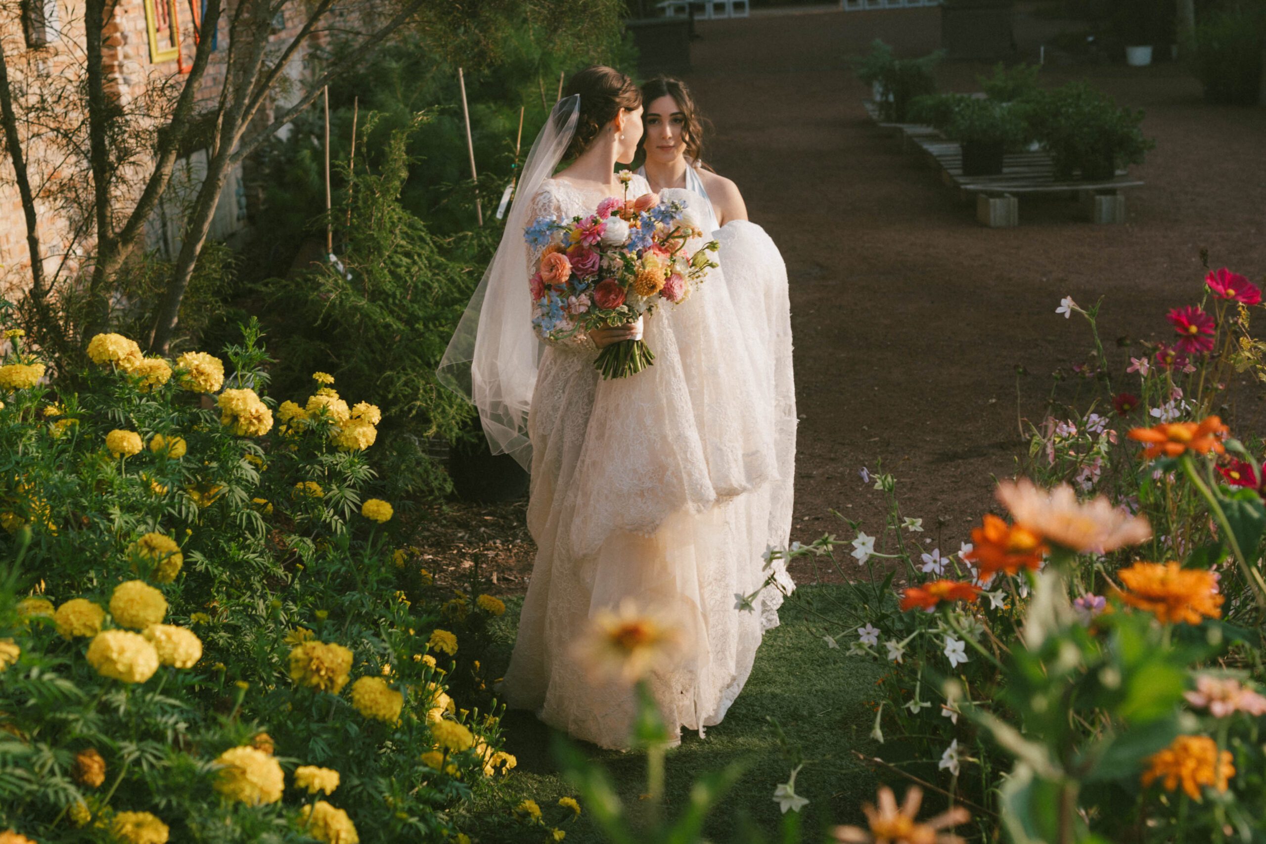 A bride walking through the garden with a bridesmaid at Blumen Gardens