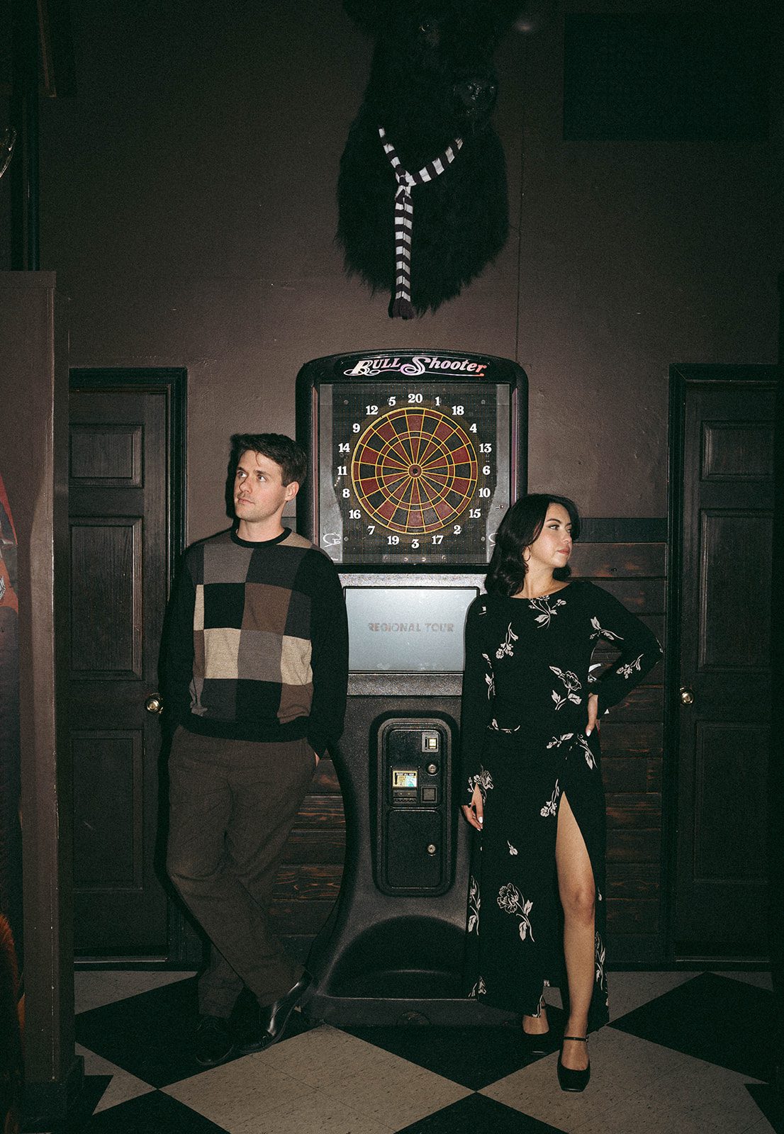 A couple standing in front of a dart machine during bar engagement photos