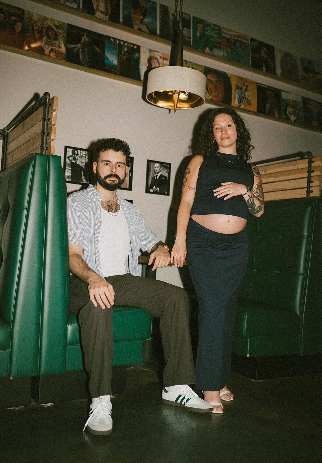 A man sitting in a restaurant booth next to his pregnant wife as maternity photoshoot ideas