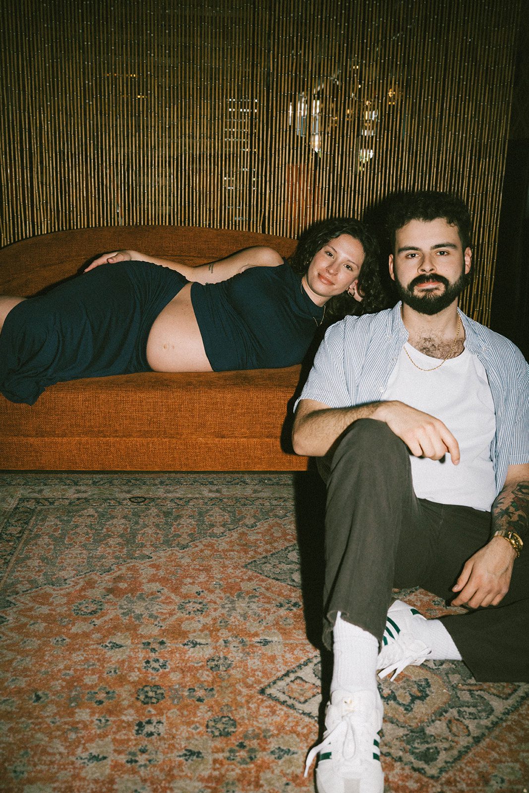 A pregnant woman lying on a couch with her husband sitting in front of her as maternity photoshoot ideas