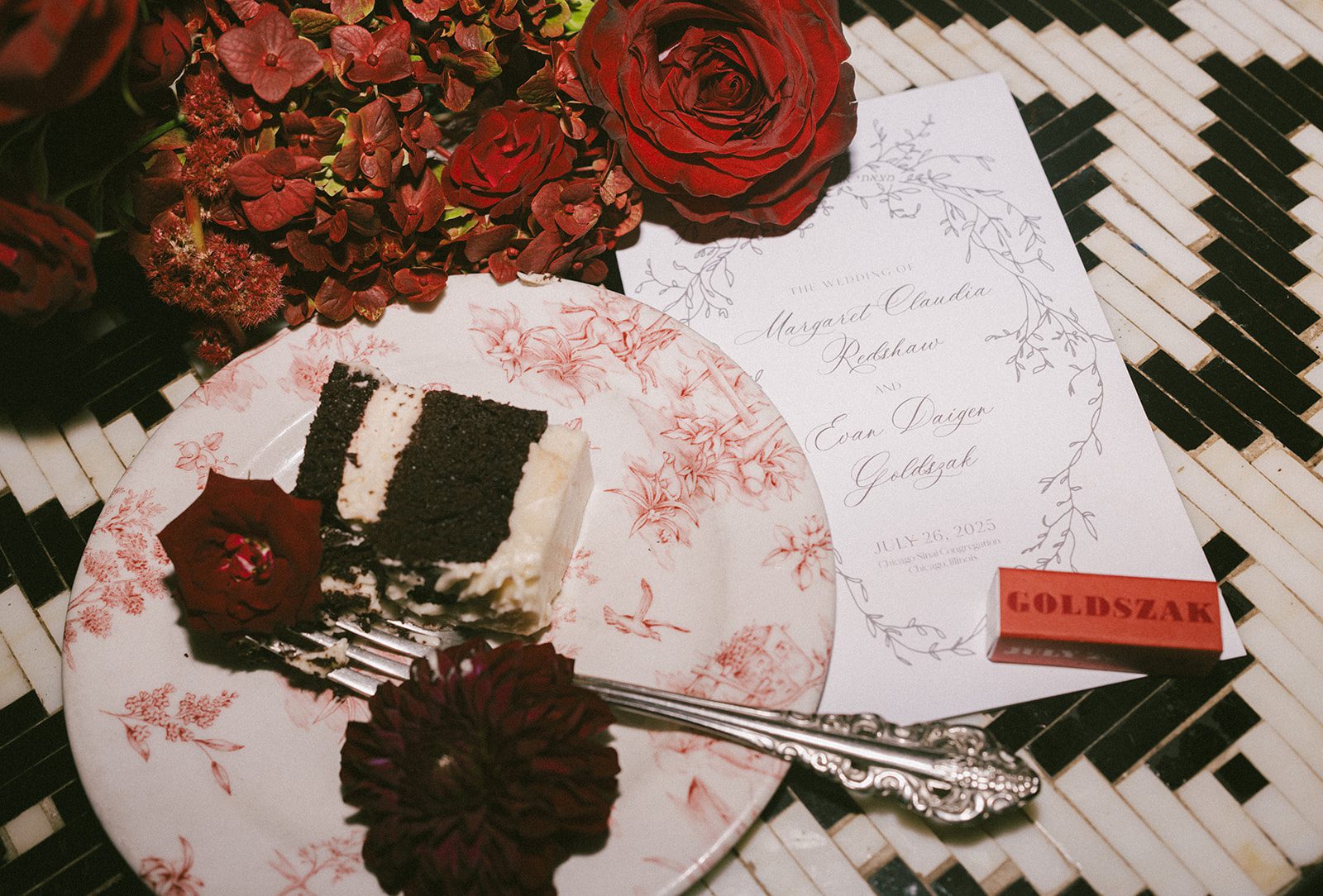 A wedding reception flatlay with chocolate cake, red flowers, and wedding invitations