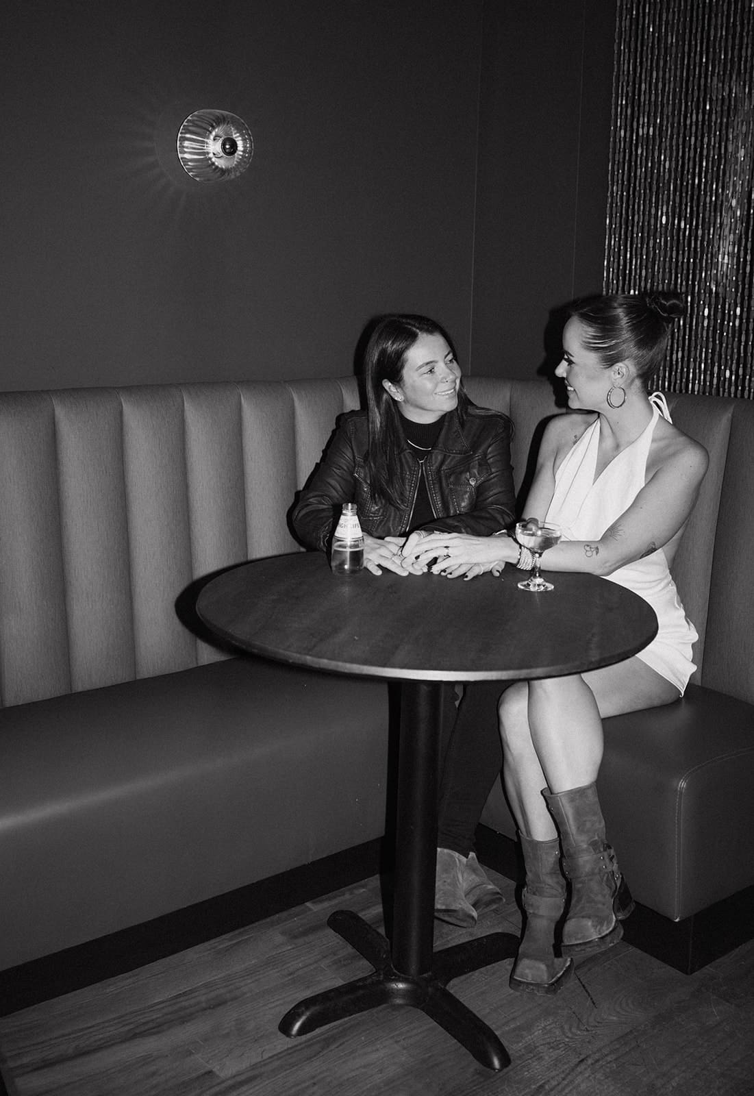 A black and white photo of a couple holding hands in a bar booth