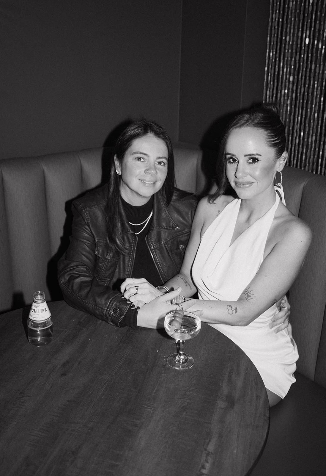A black and white photo of a couple holding hands in a bar booth