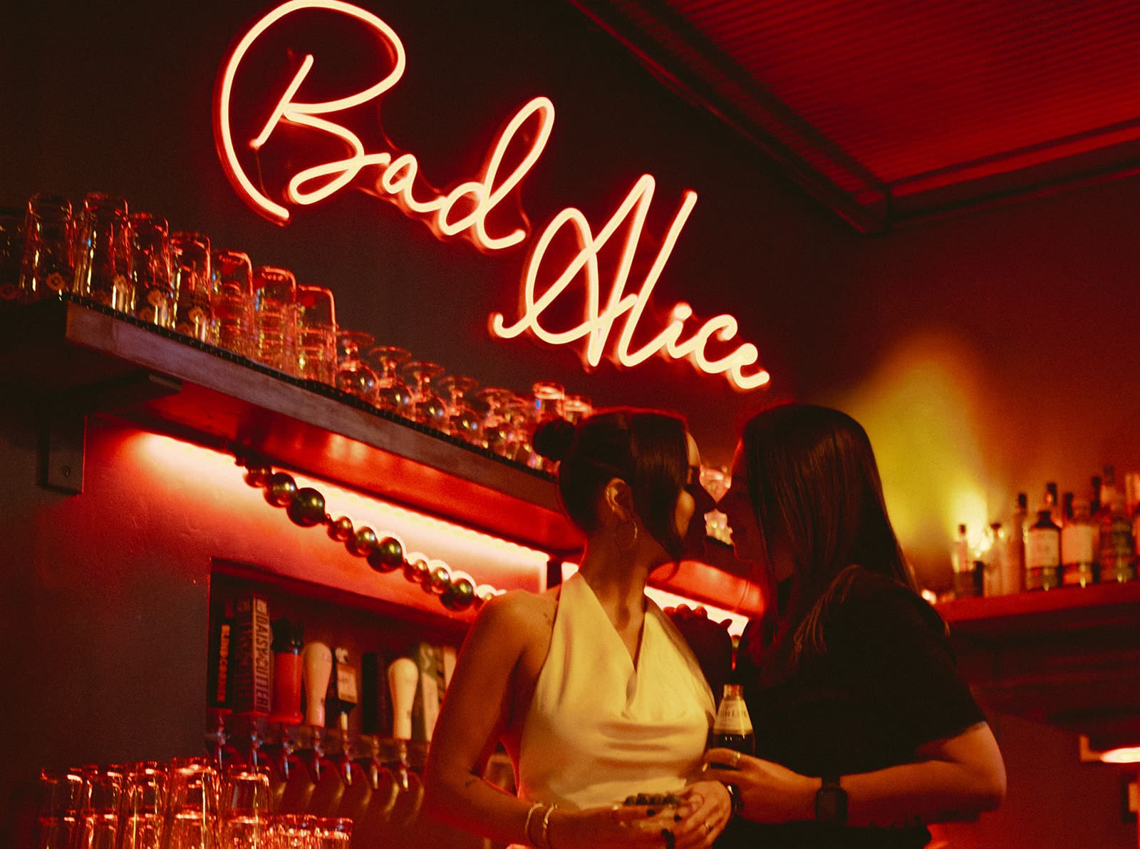 A couple leaning in for a kiss in front of a neon sign during their bar engagement photos