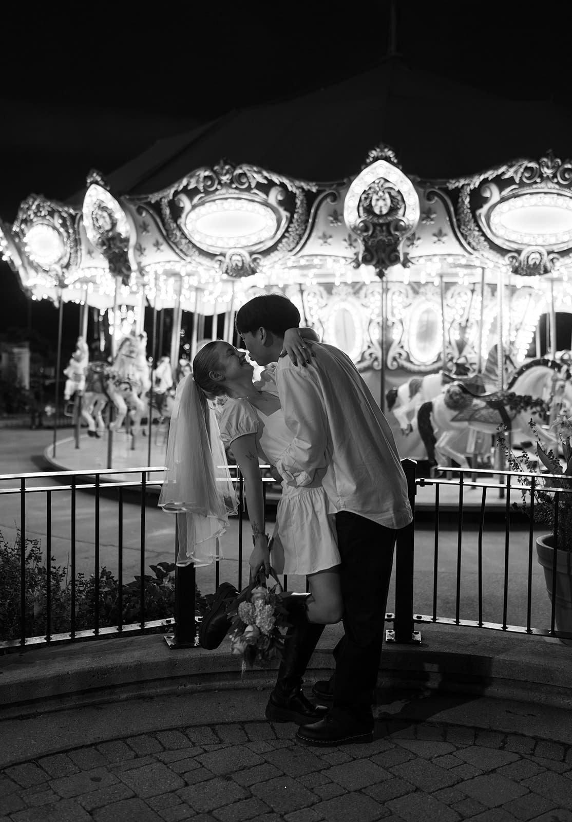 A black and white photo of a couple standing in front of a carousel for unique engagement photos