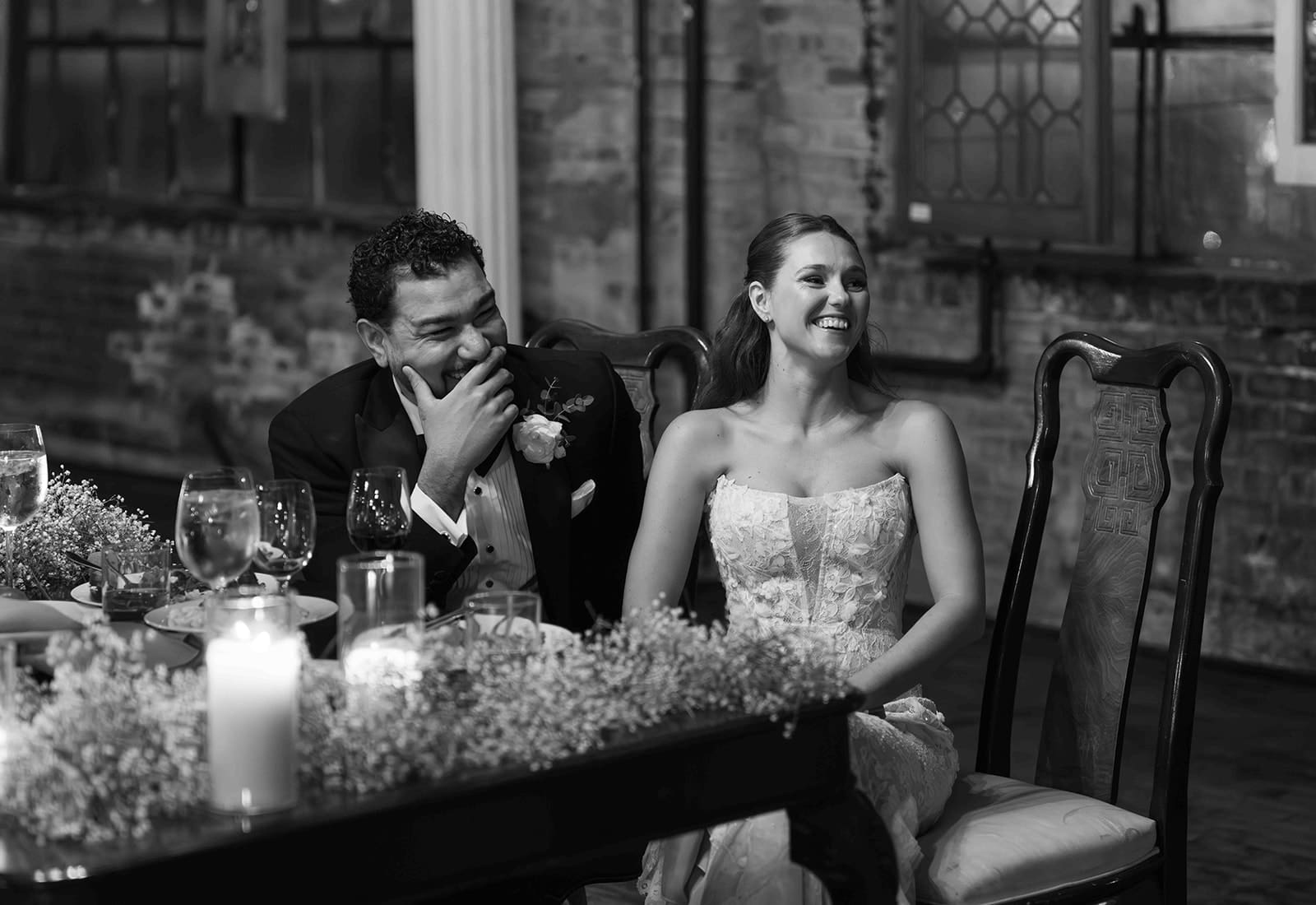 A candid photo of a bride and groom laughing during wedding toasts