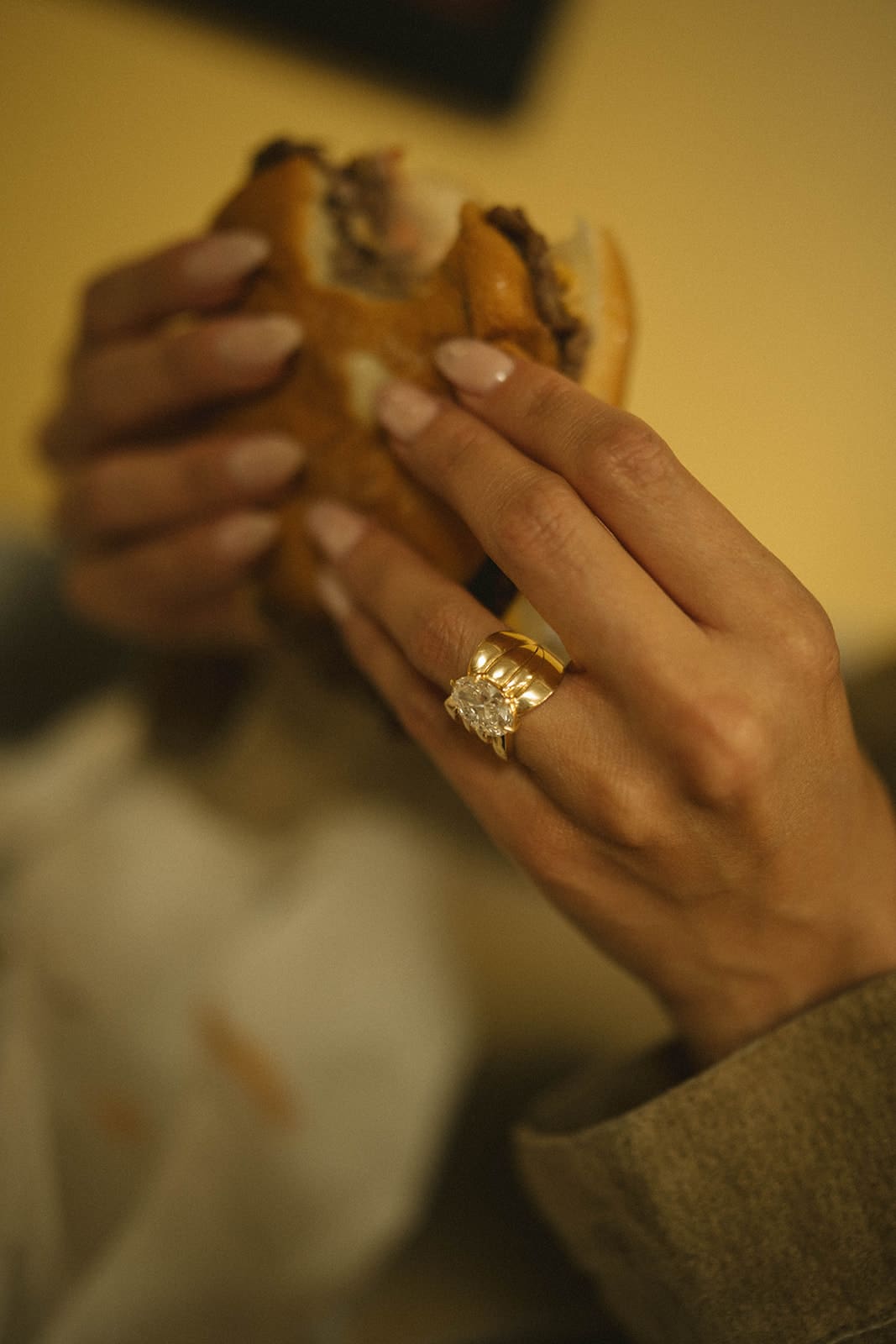 A woman showing off her engagement ring while eating a burger