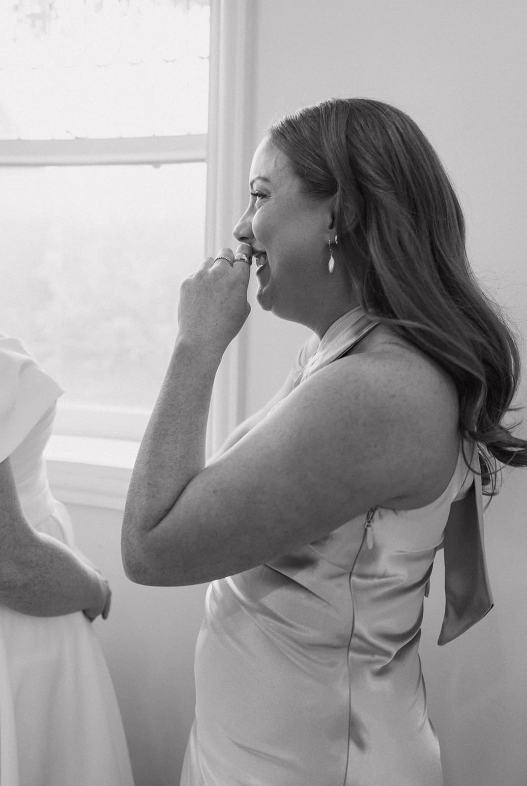 A bridesmaid laughing while helping put a veil on the bride