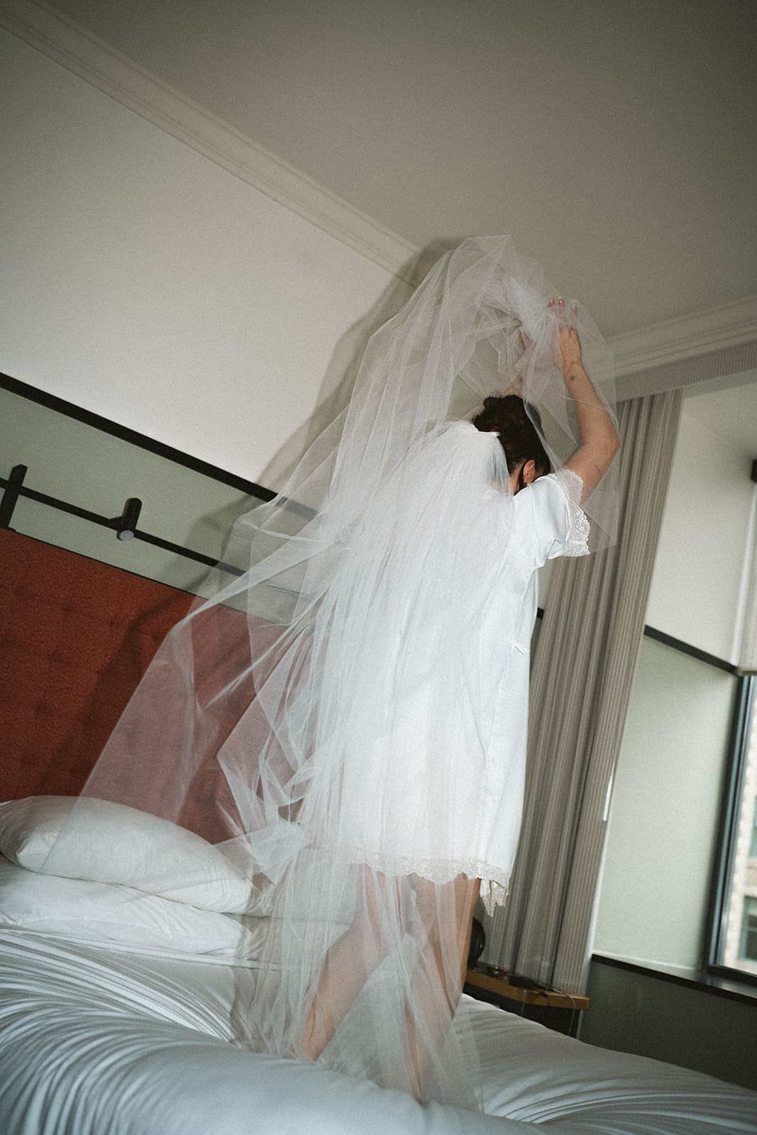 A bride dancing around on a hotel bed in her getting ready outfit
