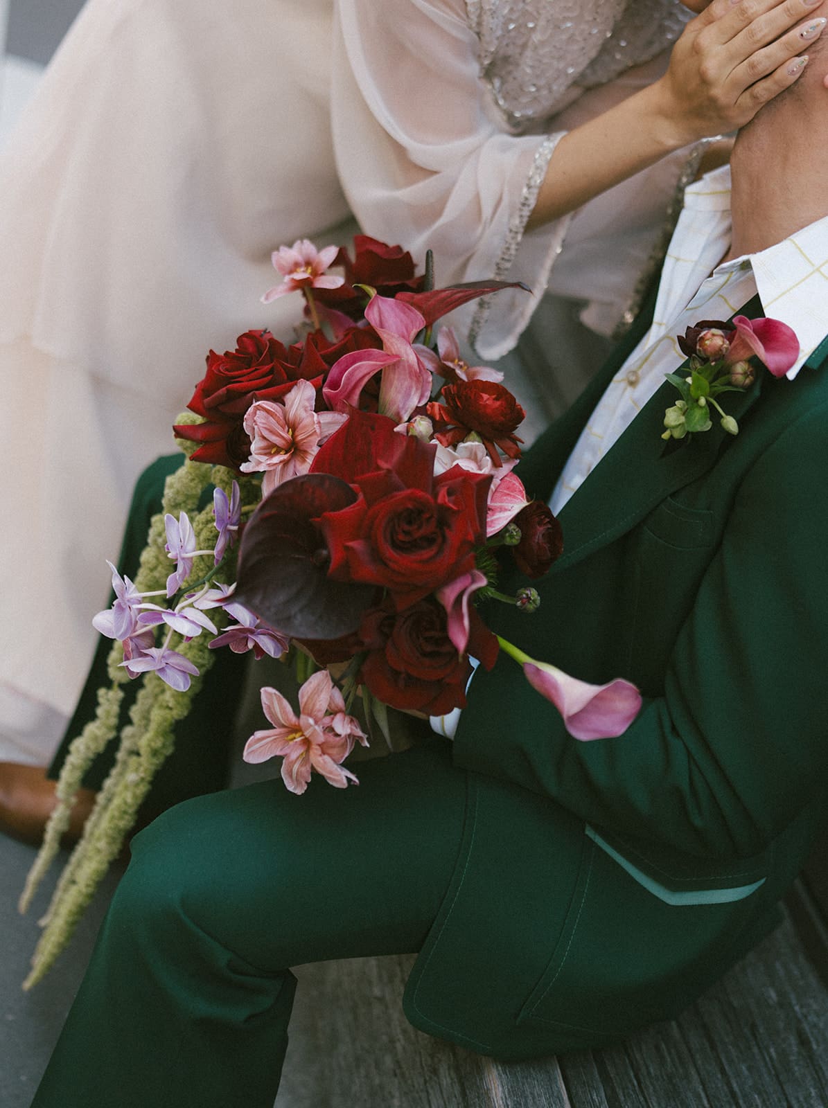 A bride holding her pink and red wedding bouquet while kissing her husband