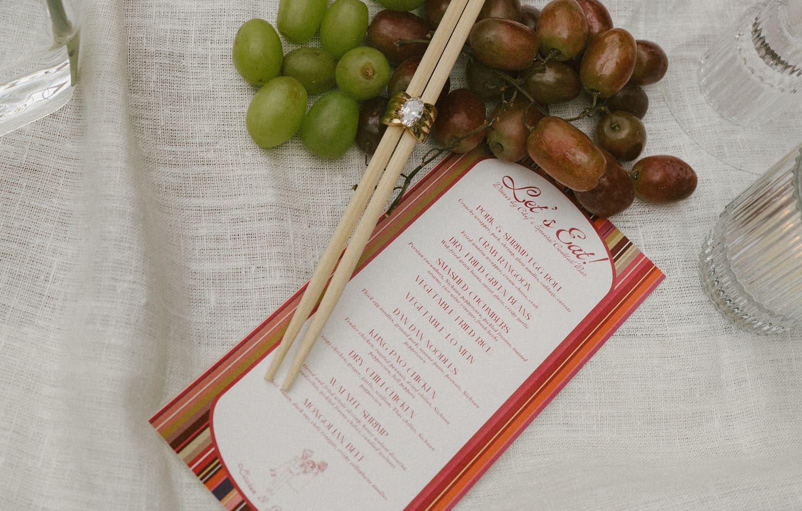 A wedding flat lay with a menu, chopsticks, and grapes