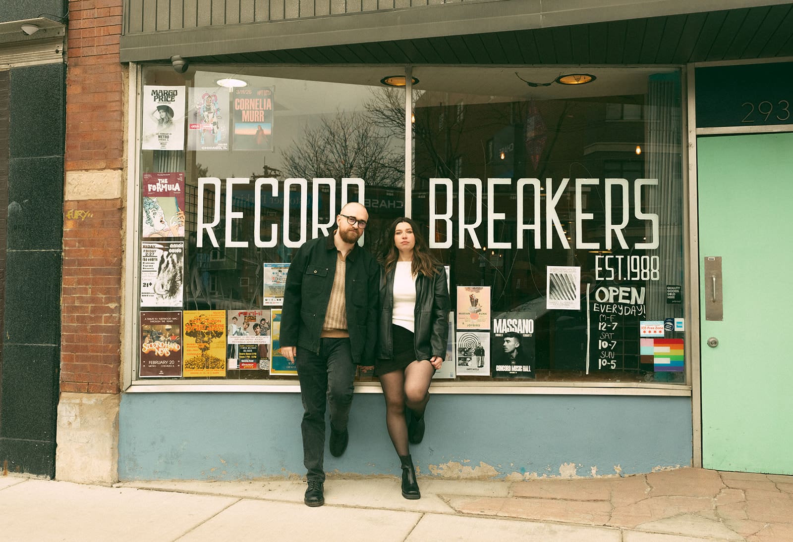 A couple posing for engagement photos in front of a record store in Logan Square
