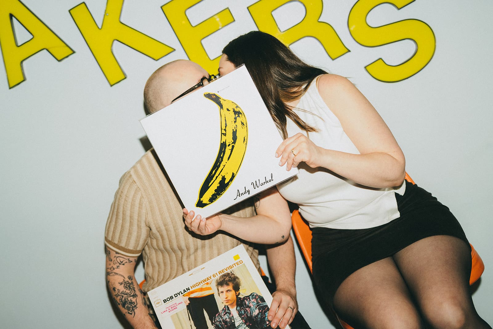 A couple kissing behind a record during a record store engagement photoshoot