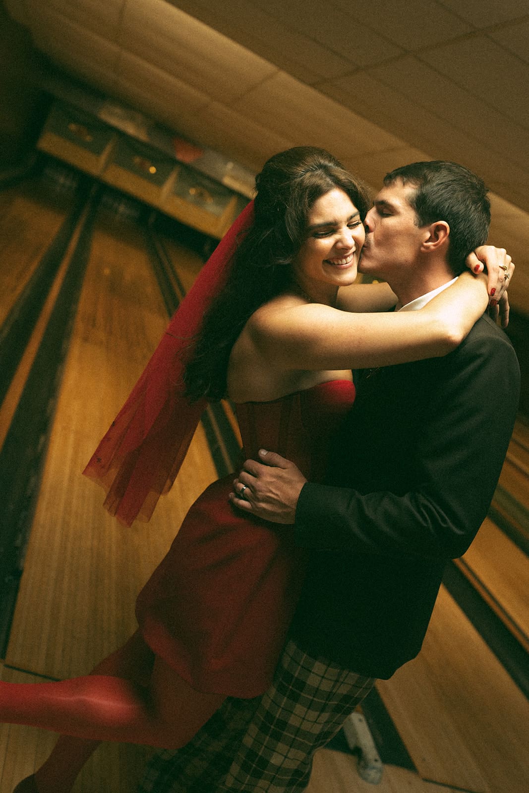 A bride and groom kissing in front of bowling lanes